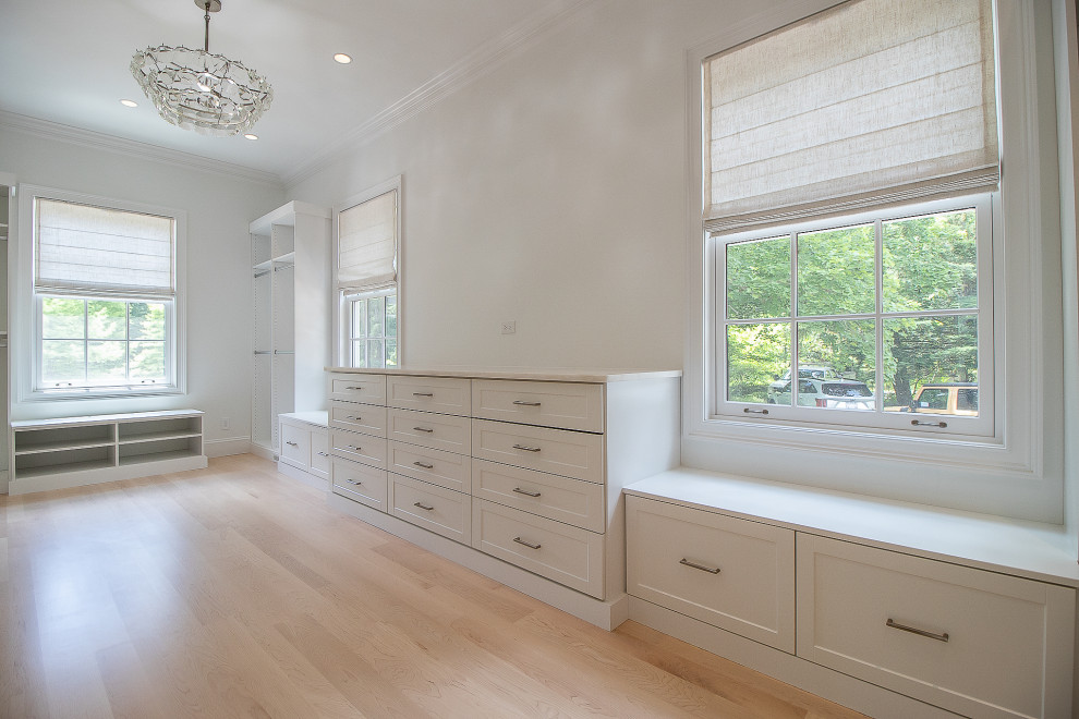 This is an example of an expansive traditional gender-neutral dressing room in Cleveland with recessed-panel cabinets, white cabinets, light hardwood floors and brown floor.