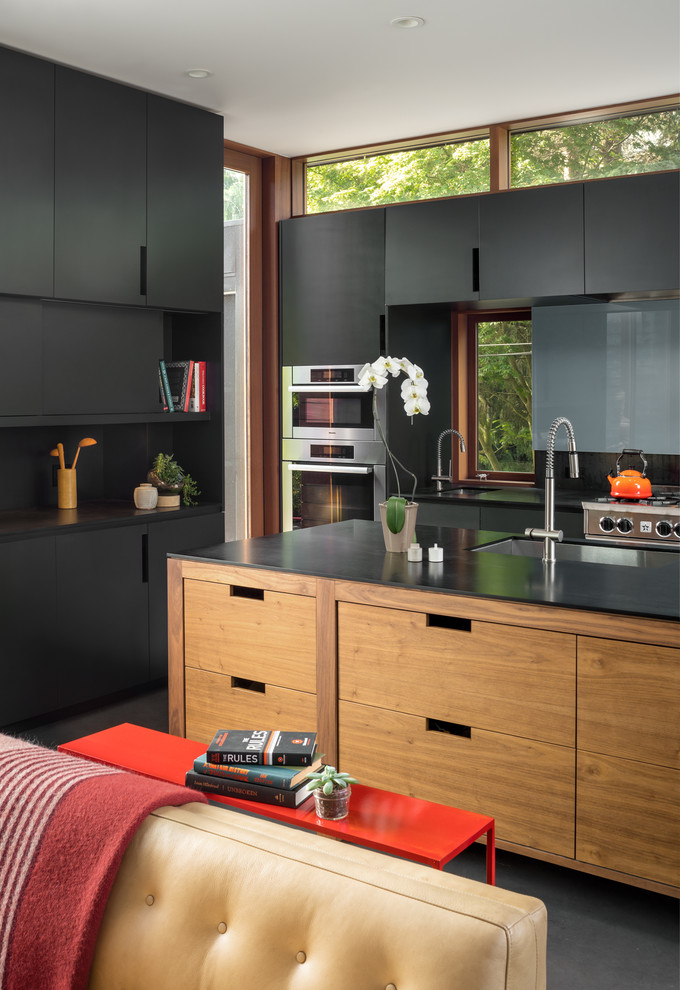 This is an example of a contemporary open plan kitchen in Seattle with an undermount sink, flat-panel cabinets, black cabinets, stainless steel appliances, with island and grey floor.