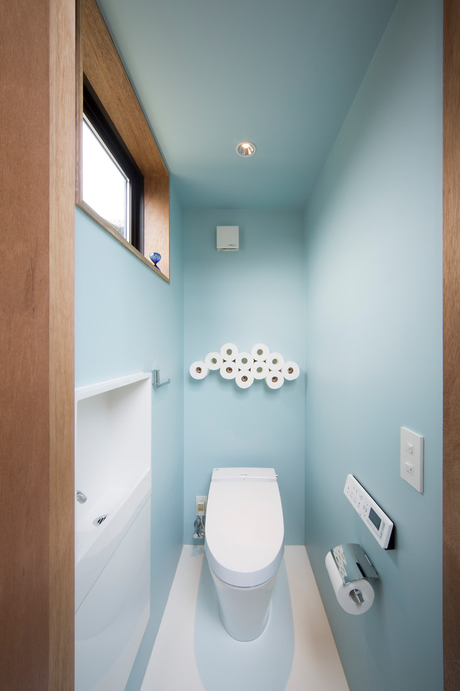 Design ideas for a modern powder room in Other with a one-piece toilet, vinyl floors, a wall-mount sink, white floor, blue walls, flat-panel cabinets and white cabinets.