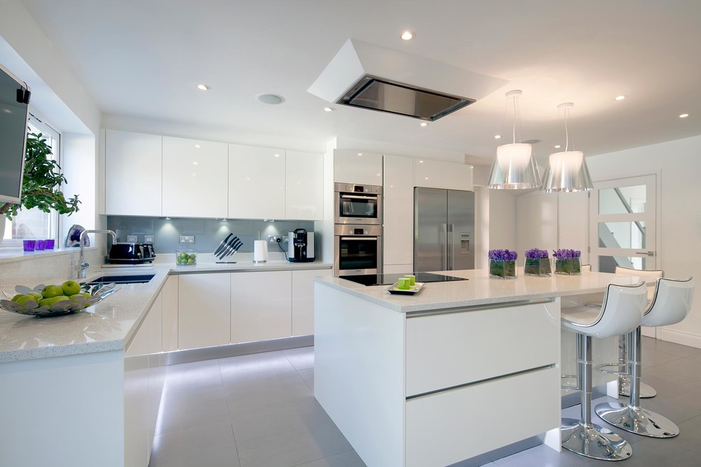 This is an example of a large contemporary l-shaped eat-in kitchen in London with an integrated sink, glass-front cabinets, white cabinets, quartzite benchtops, grey splashback, glass sheet splashback, stainless steel appliances, porcelain floors, a peninsula, grey floor and white benchtop.