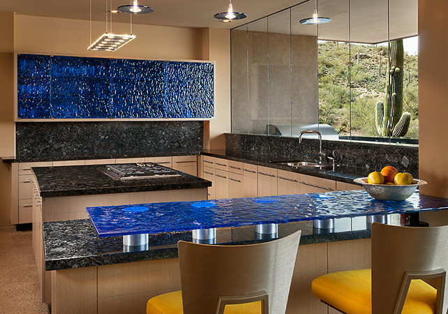 Design ideas for a modern u-shaped eat-in kitchen in Phoenix with an integrated sink, glass-front cabinets, blue cabinets, glass benchtops, black splashback, stone slab splashback and stainless steel appliances.