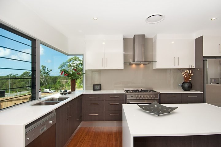 Photo of a mid-sized contemporary l-shaped kitchen pantry in Sunshine Coast with a double-bowl sink, flat-panel cabinets, dark wood cabinets, solid surface benchtops, beige splashback, glass sheet splashback, stainless steel appliances, bamboo floors and with island.