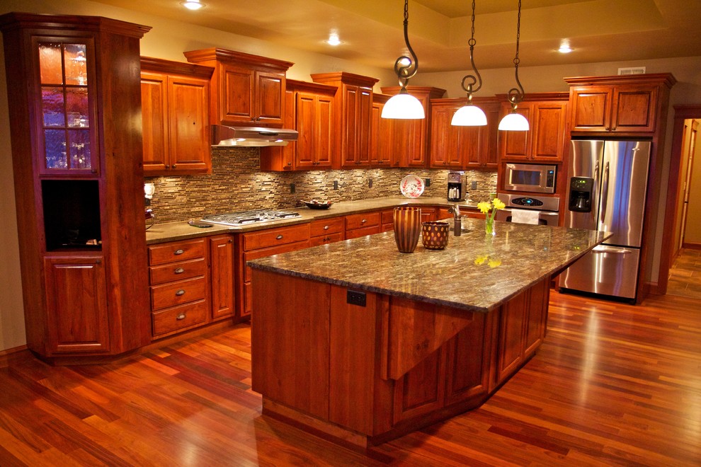 Example of a large l-shaped medium tone wood floor open concept kitchen design with an undermount sink, raised-panel cabinets, medium tone wood cabinets, multicolored backsplash, glass tile backsplash, stainless steel appliances and an island