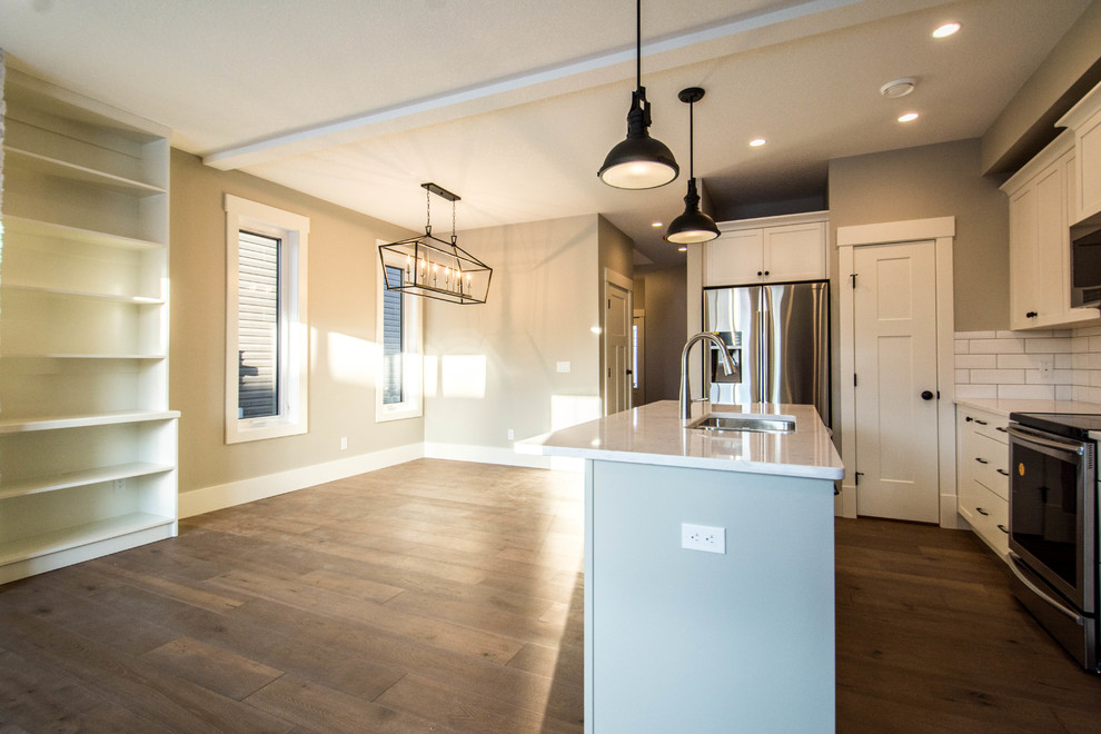 Example of a mid-sized transitional single-wall medium tone wood floor and brown floor eat-in kitchen design in Calgary with an undermount sink, shaker cabinets, gray cabinets, marble countertops, white backsplash, subway tile backsplash, stainless steel appliances, an island and white countertops