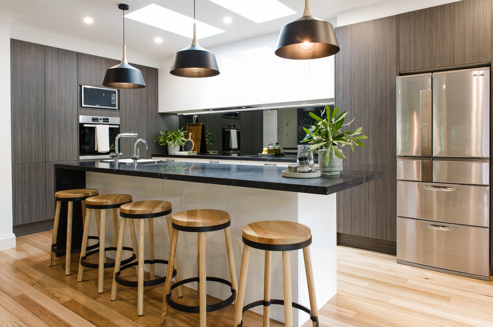 This is an example of a large modern u-shaped kitchen in Melbourne with an undermount sink, white cabinets, solid surface benchtops, glass sheet splashback, stainless steel appliances, medium hardwood floors and with island.
