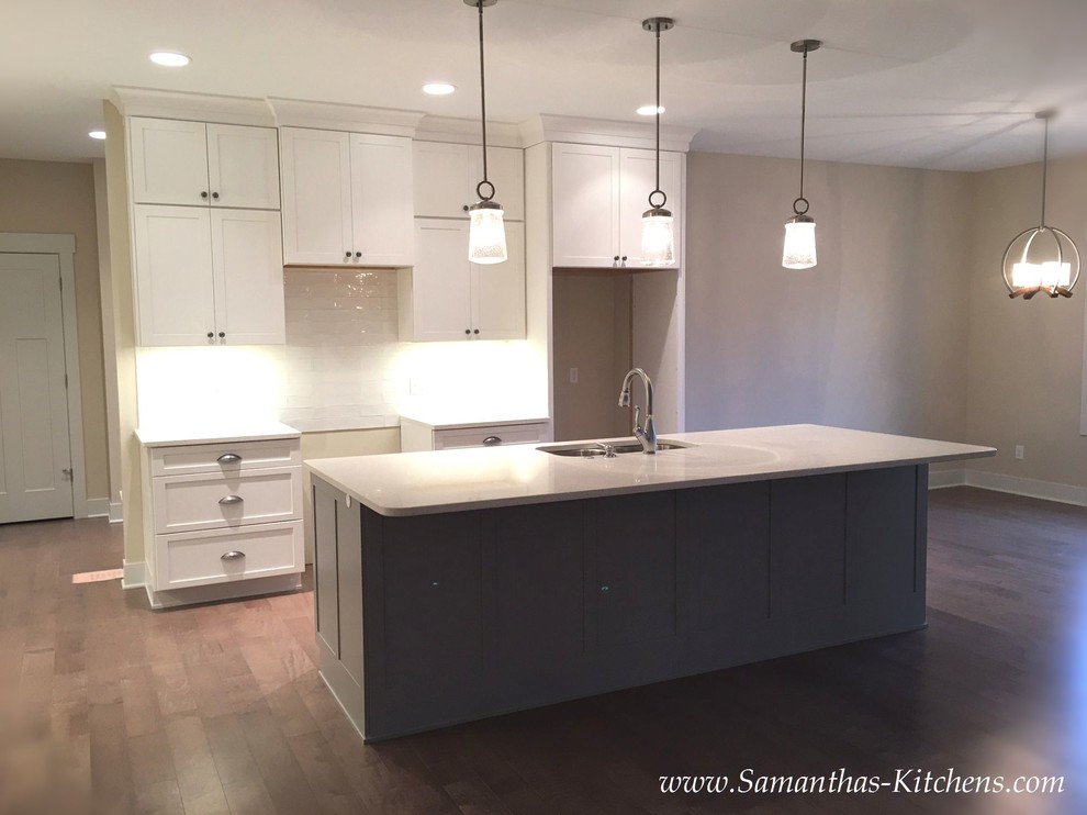 Example of a mid-sized transitional l-shaped medium tone wood floor eat-in kitchen design with an undermount sink, shaker cabinets, white cabinets, quartz countertops, white backsplash, subway tile backsplash and an island