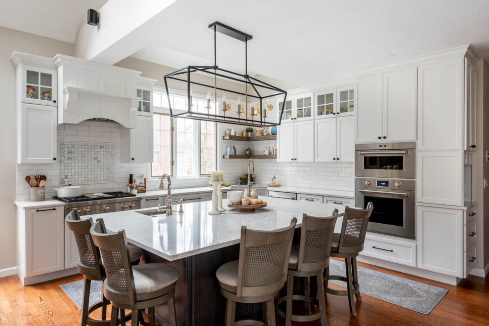 Expansive transitional l-shaped open plan kitchen in Boston with an undermount sink, shaker cabinets, white cabinets, quartz benchtops, white splashback, subway tile splashback, stainless steel appliances, dark hardwood floors, with island, brown floor, white benchtop and vaulted.