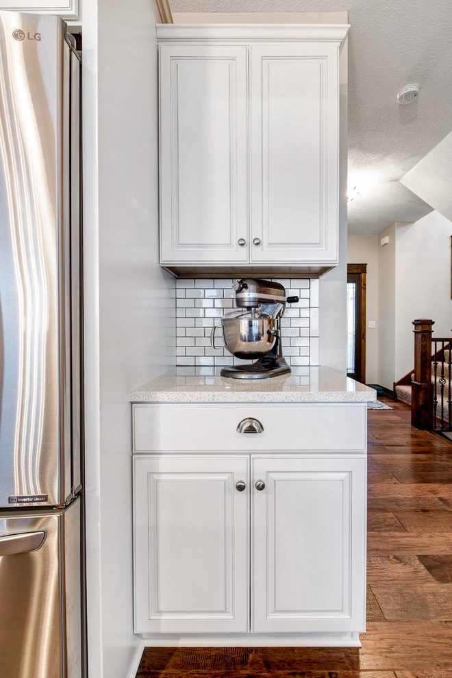 This is an example of a transitional kitchen pantry in Minneapolis with an undermount sink, raised-panel cabinets, white cabinets, quartz benchtops, white splashback, subway tile splashback, stainless steel appliances, medium hardwood floors and with island.