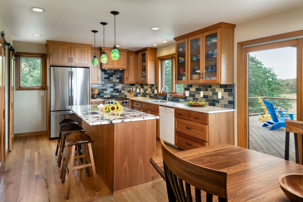 This is an example of a mid-sized arts and crafts u-shaped eat-in kitchen in Other with an undermount sink, shaker cabinets, medium wood cabinets, granite benchtops, blue splashback, ceramic splashback, stainless steel appliances, medium hardwood floors, with island, brown floor and multi-coloured benchtop.
