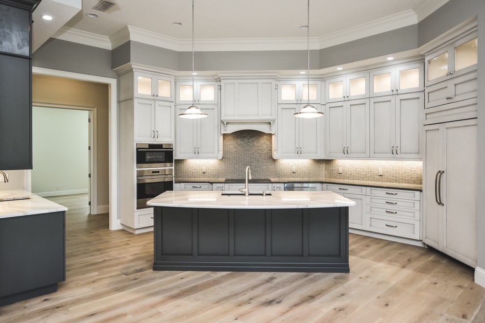 This is an example of a large transitional u-shaped eat-in kitchen in Tampa with a single-bowl sink, shaker cabinets, white cabinets, quartz benchtops, grey splashback, glass tile splashback, panelled appliances, light hardwood floors and with island.