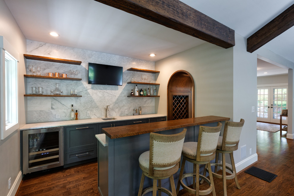 Photo of a transitional galley seated home bar in Cincinnati with shaker cabinets, blue cabinets, wood benchtops, brown floor, an undermount sink, grey splashback, marble splashback, medium hardwood floors and white benchtop.