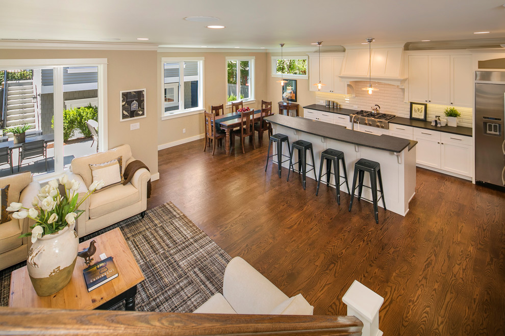 Example of a classic galley medium tone wood floor eat-in kitchen design in Seattle with a farmhouse sink, shaker cabinets, white cabinets, granite countertops, gray backsplash, subway tile backsplash, stainless steel appliances and an island