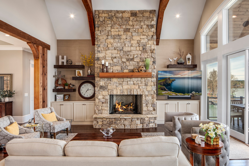 Photo of a mid-sized country formal open concept living room in Other with beige walls, medium hardwood floors, a standard fireplace, a stone fireplace surround, a wall-mounted tv and brown floor.