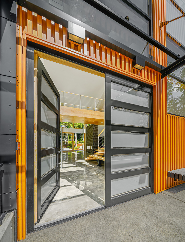 Стильный дизайн: входная дверь среднего размера в стиле модернизм с оранжевыми стенами, бетонным полом, двустворчатой входной дверью, черной входной дверью, серым полом, любым потолком и панелями на части стены - последний тренд