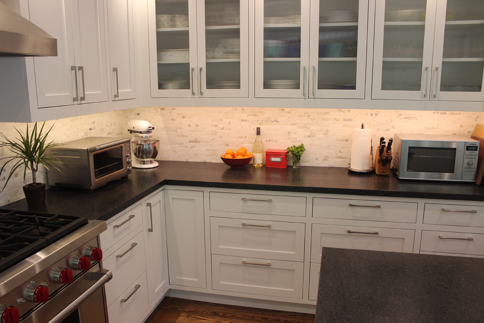 Inspiration for a mid-sized transitional l-shaped eat-in kitchen in San Francisco with shaker cabinets, white cabinets, white splashback, mosaic tile splashback, stainless steel appliances, medium hardwood floors, with island, a farmhouse sink and solid surface benchtops.