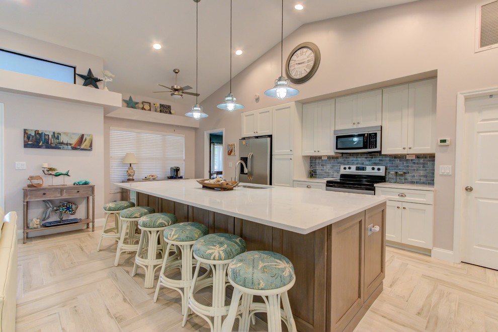 Open concept kitchen - large single-wall porcelain tile and white floor open concept kitchen idea with an undermount sink, shaker cabinets, white cabinets, quartz countertops, blue backsplash, stainless steel appliances, an island and white countertops