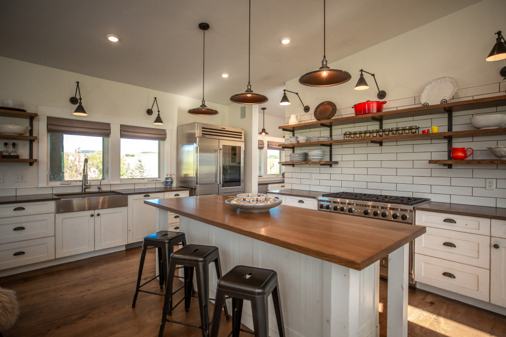 Inspiration for a cottage kitchen remodel with a farmhouse sink, shaker cabinets, white cabinets, subway tile backsplash, stainless steel appliances and an island