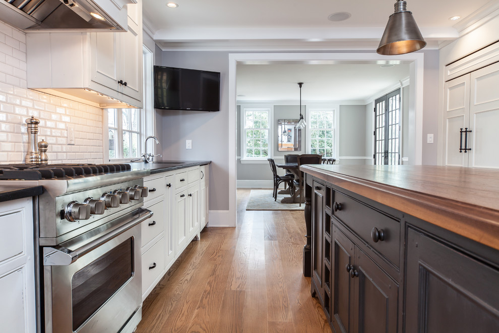 Photo of a large transitional l-shaped eat-in kitchen in Philadelphia with a single-bowl sink, recessed-panel cabinets, white cabinets, white splashback, subway tile splashback, stainless steel appliances, light hardwood floors, with island, brown floor, soapstone benchtops and black benchtop.