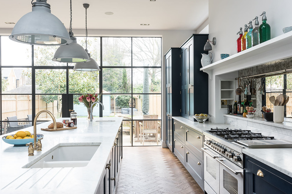 Large traditional galley eat-in kitchen in London with shaker cabinets, blue cabinets, marble benchtops, panelled appliances, medium hardwood floors, with island and an undermount sink.