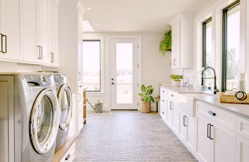 Photo of a country galley laundry room in Portland with a farmhouse sink, shaker cabinets, white cabinets, grey walls, grey floor and grey benchtop.