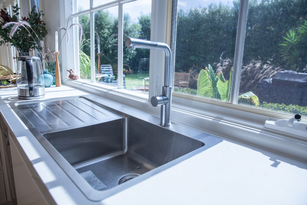 Photo of a mid-sized scandinavian u-shaped eat-in kitchen in Melbourne with an undermount sink, flat-panel cabinets, white cabinets, granite benchtops, white splashback, glass sheet splashback, a peninsula, stainless steel appliances, light hardwood floors and grey benchtop.