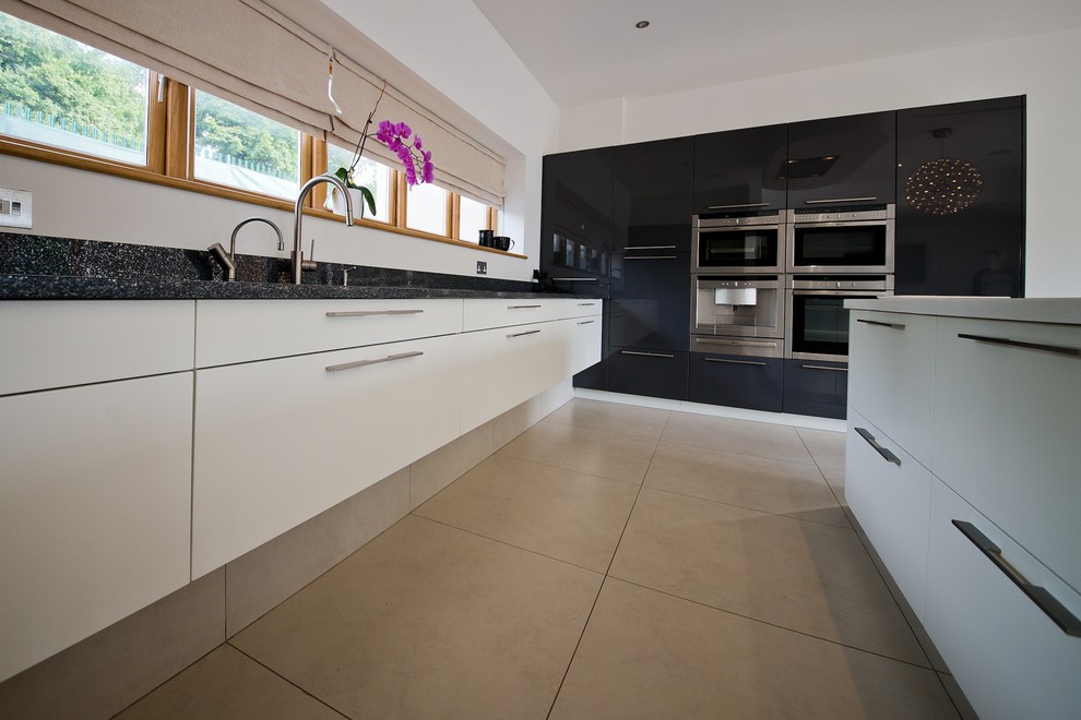This is an example of a large contemporary eat-in kitchen in Cardiff with an undermount sink, white cabinets, solid surface benchtops, travertine floors and with island.