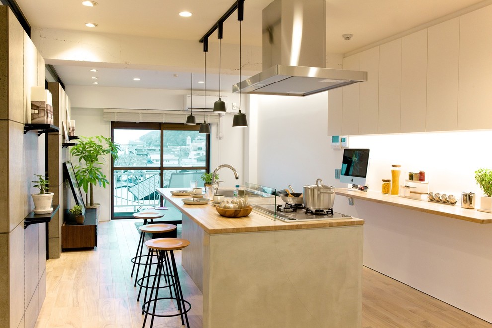 Design ideas for a contemporary single-wall kitchen in Other with flat-panel cabinets, white cabinets, wood benchtops, white splashback, light hardwood floors and with island.