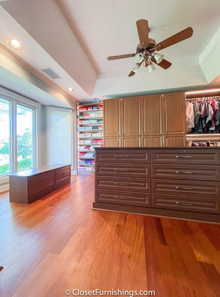 This is an example of a large traditional women's walk-in wardrobe in Chicago with raised-panel cabinets and brown cabinets.