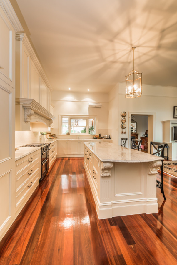 Inspiration for an expansive traditional l-shaped open plan kitchen in Adelaide with a double-bowl sink, beaded inset cabinets, distressed cabinets, granite benchtops, white splashback, ceramic splashback, black appliances, white walls, medium hardwood floors and with island.