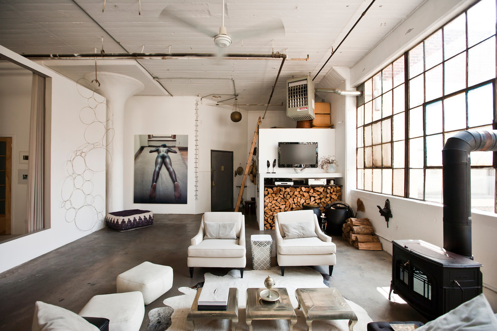 Expansive industrial open concept living room in New York with white walls and a wood stove.