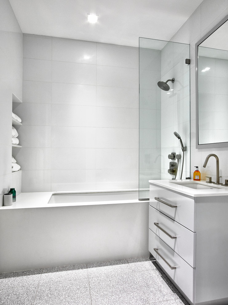 Inspiration for a mid-sized contemporary bathroom in New York with flat-panel cabinets, white cabinets, an undermount tub, a shower/bathtub combo, a one-piece toilet, white tile, glass tile, white walls, ceramic floors, an undermount sink and engineered quartz benchtops.