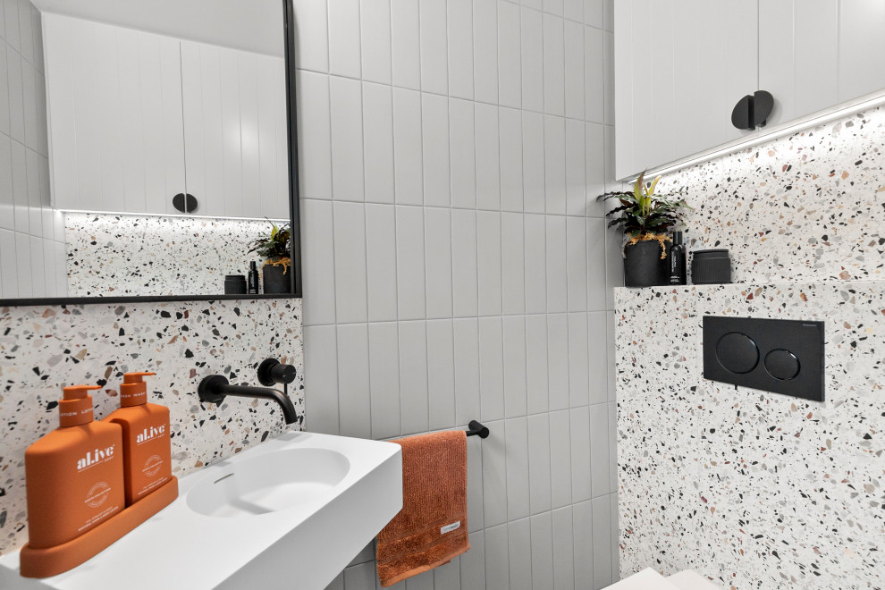 シドニーにある高級な小さなコンテンポラリースタイルのおしゃれなトイレ・洗面所 (白いキャビネット、一体型トイレ	、グレーのタイル、サブウェイタイル、マルチカラーの壁、テラゾーの床、壁付け型シンク、人工大理石カウンター、マルチカラーの床、白い洗面カウンター、フローティング洗面台) の写真