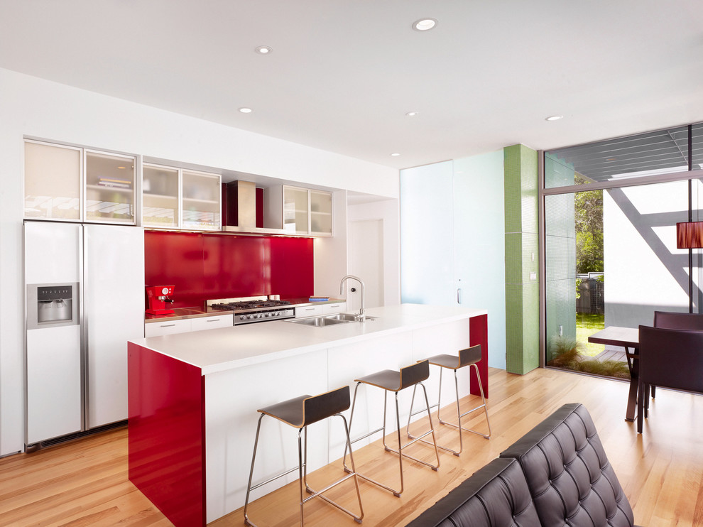 Design ideas for a modern galley open plan kitchen in Austin with glass-front cabinets, concrete benchtops, a drop-in sink, red splashback, metal splashback and white appliances.