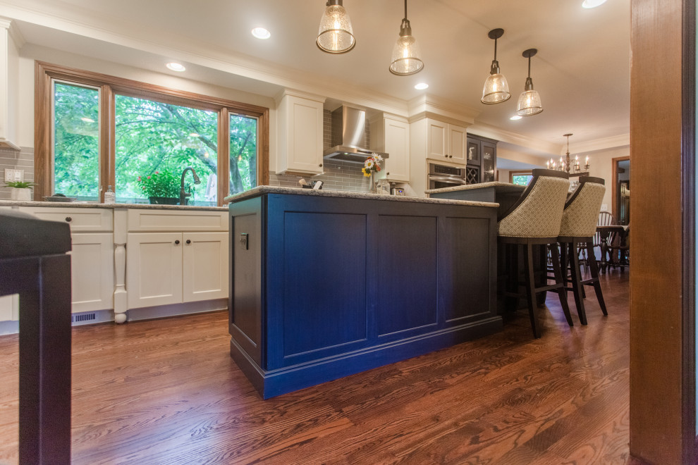 Eat-in kitchen - large transitional single-wall dark wood floor, brown floor and coffered ceiling eat-in kitchen idea in Cincinnati with a double-bowl sink, shaker cabinets, white cabinets, granite countertops, gray backsplash, subway tile backsplash, stainless steel appliances, an island and multicolored countertops