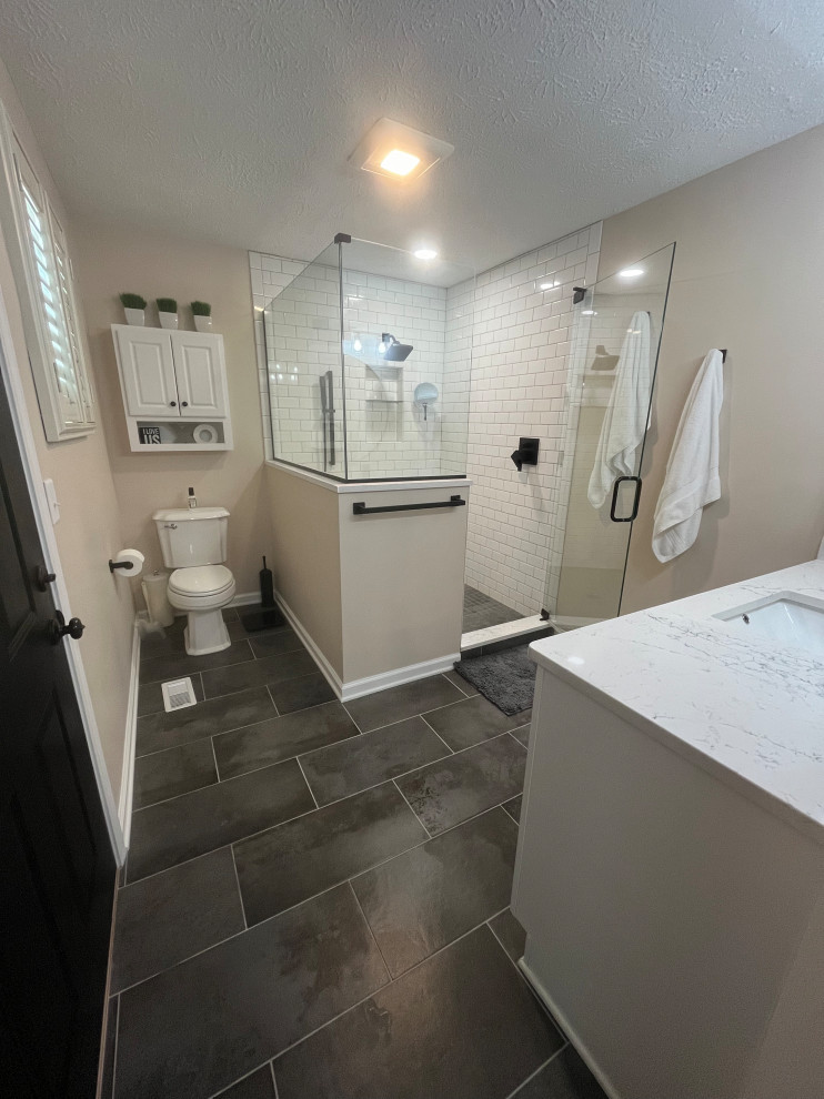 Cette image montre une salle de bain principale rustique de taille moyenne avec un placard à porte shaker, des portes de placard blanches, une douche d'angle, WC séparés, un carrelage blanc, un carrelage métro, un mur beige, un sol en carrelage de porcelaine, un lavabo encastré, un plan de toilette en quartz, un sol gris, une cabine de douche à porte battante, un plan de toilette blanc, une niche, meuble simple vasque et meuble-lavabo encastré.
