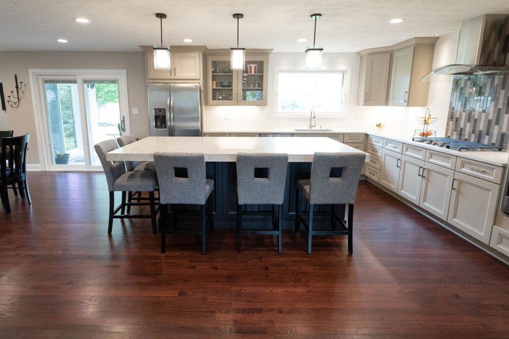 This is an example of a mid-sized transitional l-shaped eat-in kitchen in Cleveland with an undermount sink, recessed-panel cabinets, grey cabinets, quartz benchtops, white splashback, porcelain splashback, stainless steel appliances, medium hardwood floors, with island, red floor and white benchtop.