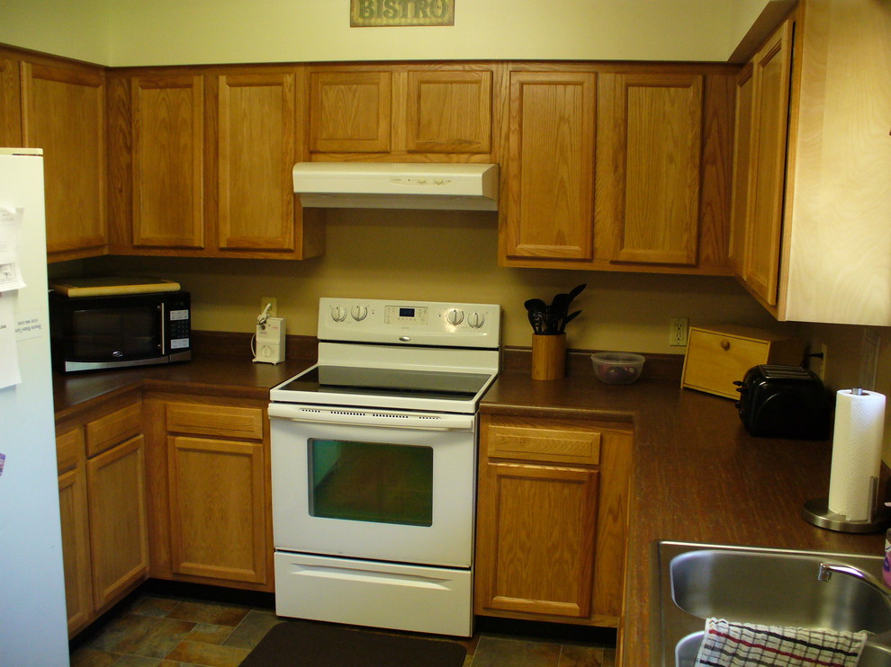 This is an example of a mid-sized traditional u-shaped eat-in kitchen in Detroit with a double-bowl sink, flat-panel cabinets, light wood cabinets, laminate benchtops, beige splashback, white appliances, ceramic floors and no island.