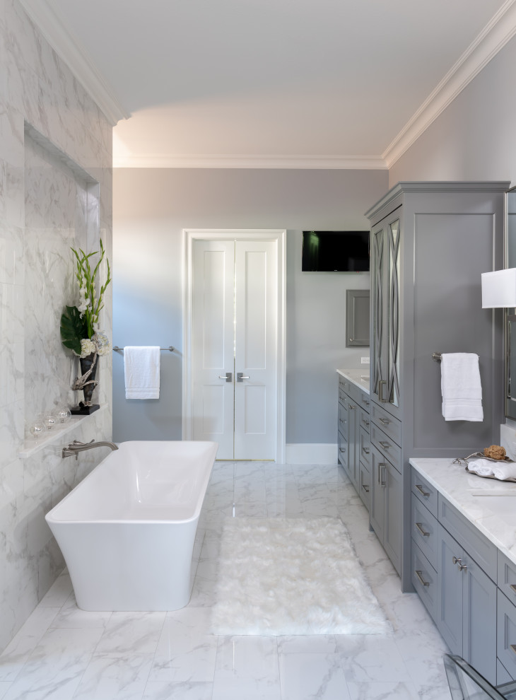 Example of a huge transitional master white tile and porcelain tile porcelain tile, white floor and double-sink freestanding bathtub design with shaker cabinets, gray cabinets, a one-piece toilet, gray walls, an undermount sink, marble countertops, a hinged shower door, white countertops and a built-in vanity