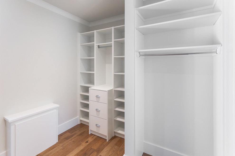 This is an example of a mid-sized modern gender-neutral walk-in wardrobe with shaker cabinets, white cabinets, medium hardwood floors and brown floor.