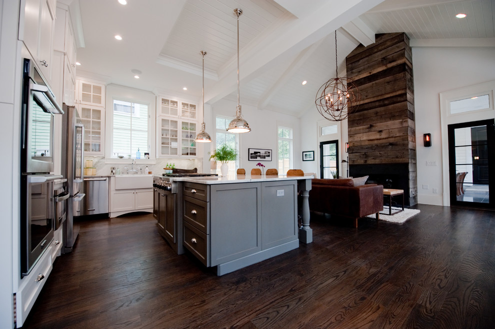 This is an example of a large transitional l-shaped eat-in kitchen in Atlanta with with island, shaker cabinets, white cabinets, marble benchtops, white splashback, stone slab splashback, stainless steel appliances, a farmhouse sink, dark hardwood floors and brown floor.