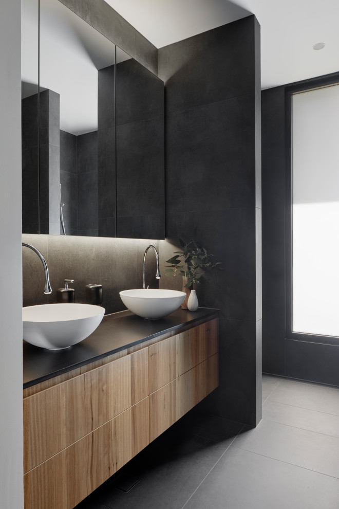 Photo of a mid-sized contemporary master bathroom in Melbourne with flat-panel cabinets, medium wood cabinets, black tile, ceramic tile, ceramic floors, a vessel sink, engineered quartz benchtops, black benchtops, grey floor, a double vanity and a floating vanity.