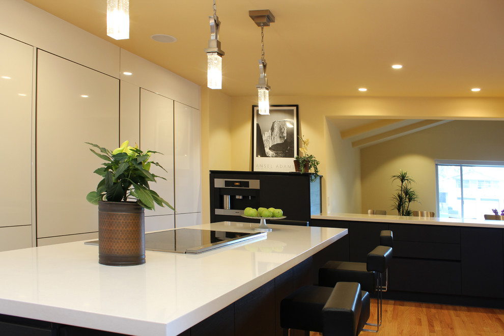 This is an example of a contemporary u-shaped kitchen in San Francisco with an undermount sink, flat-panel cabinets, white cabinets, quartz benchtops, panelled appliances, light hardwood floors and multiple islands.