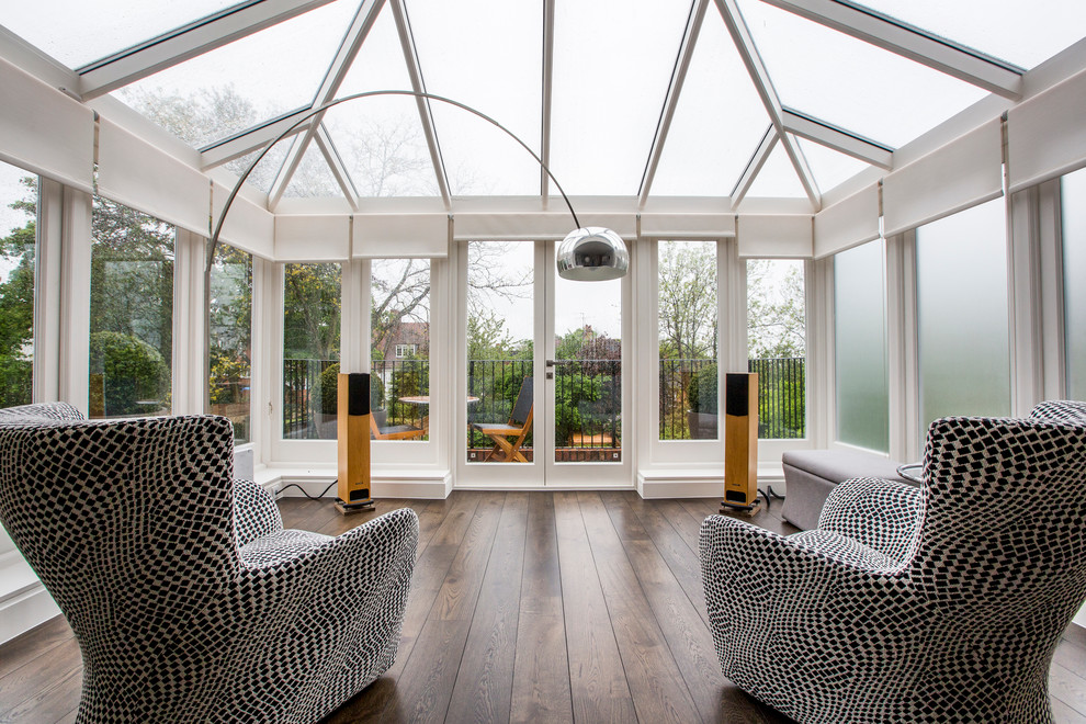 This is an example of a mid-sized contemporary sunroom in London with dark hardwood floors, no fireplace and a glass ceiling.