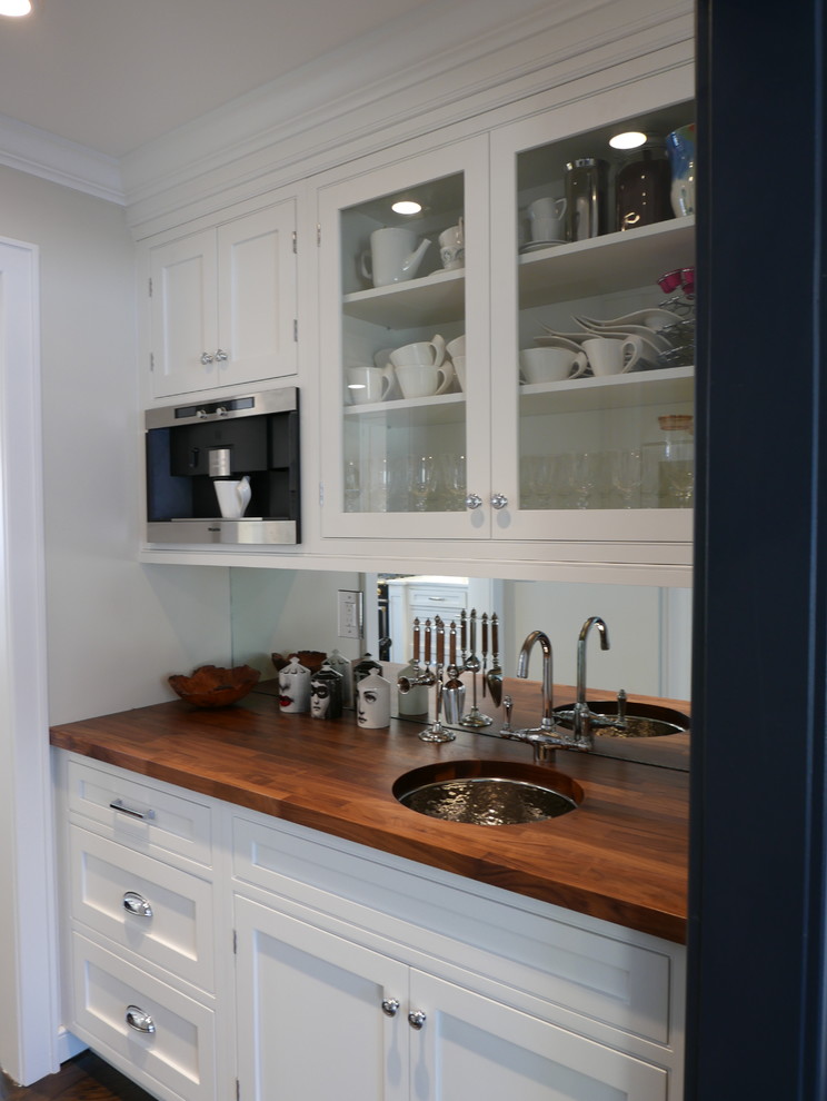 This is an example of a small transitional single-wall kitchen pantry in New York with an undermount sink, recessed-panel cabinets, white cabinets, wood benchtops, mirror splashback, stainless steel appliances, dark hardwood floors and with island.