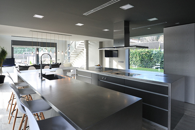 Modelo de cocina actual grande abierta con fregadero integrado, armarios abiertos, puertas de armario en acero inoxidable, electrodomésticos de acero inoxidable, suelo de madera en tonos medios y una isla