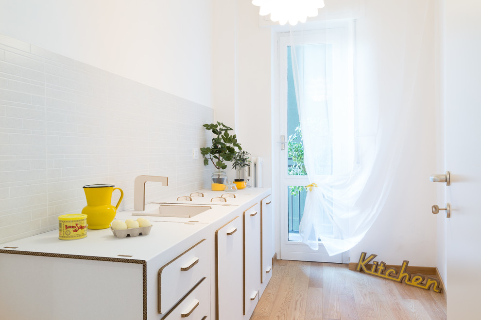This is an example of a small scandinavian galley separate kitchen in Milan with an undermount sink, recessed-panel cabinets, white cabinets, white splashback, medium hardwood floors, no island and beige floor.