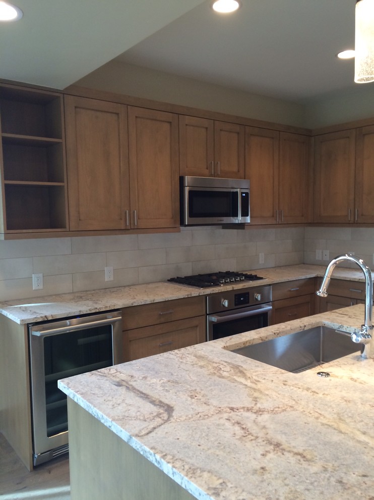 Inspiration for a small transitional l-shaped medium tone wood floor kitchen remodel with an undermount sink, shaker cabinets, medium tone wood cabinets, granite countertops, beige backsplash, porcelain backsplash, stainless steel appliances and an island
