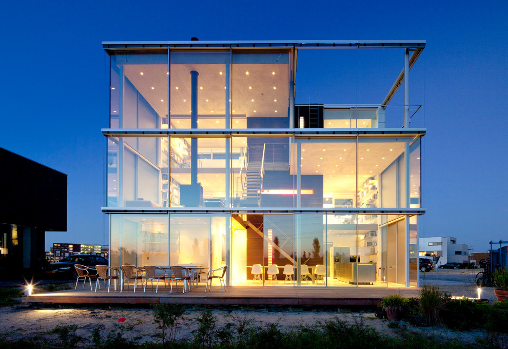 Esempio della villa grande moderna a tre piani con rivestimento in vetro, tetto piano e copertura verde