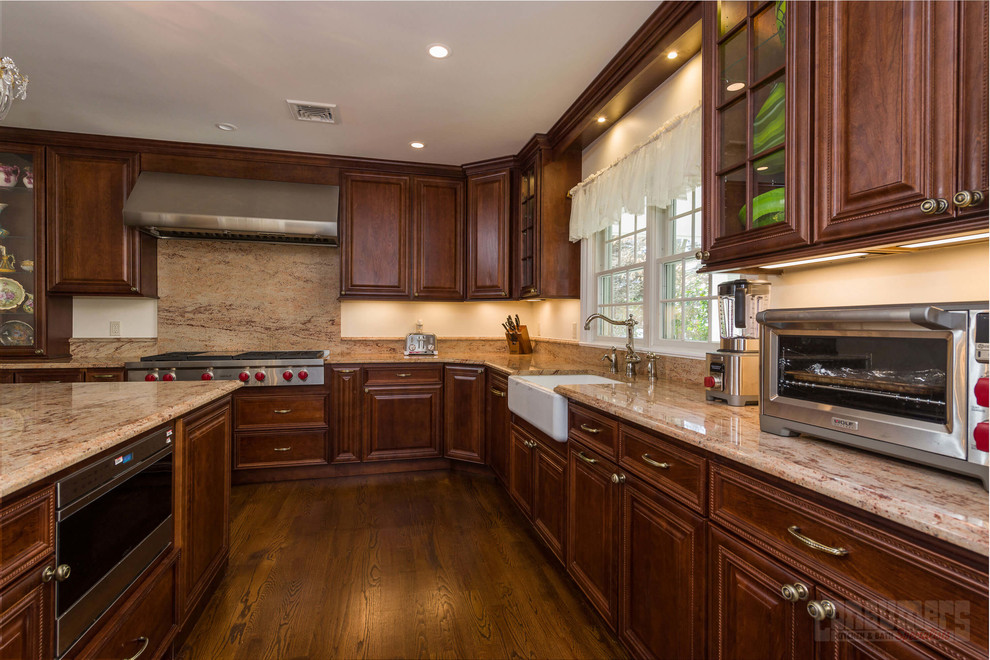 Expansive u-shaped eat-in kitchen in New York with a farmhouse sink, raised-panel cabinets, brown cabinets, beige splashback, stainless steel appliances, plywood floors and with island.