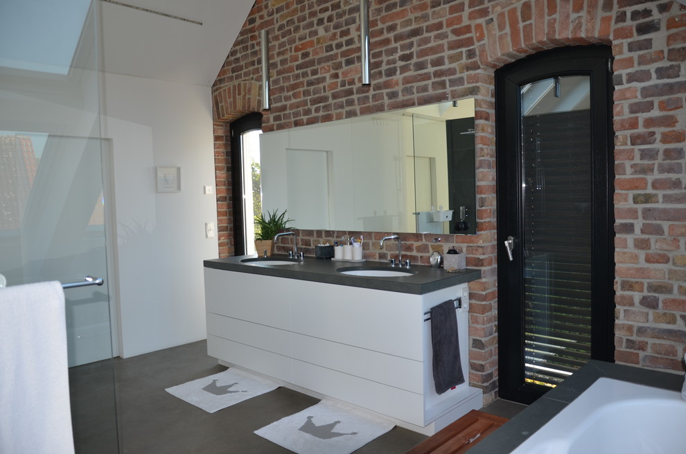Mid-sized contemporary bathroom in Dusseldorf with white walls, concrete floors, grey floor, white cabinets, an integrated sink, granite benchtops, grey benchtops, a double vanity and brick walls.